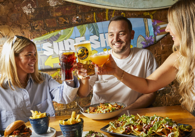 image of 3 guests at a table with food and cheers-ing drinks image of 3 guests at a table with food and cheers-ing drinks